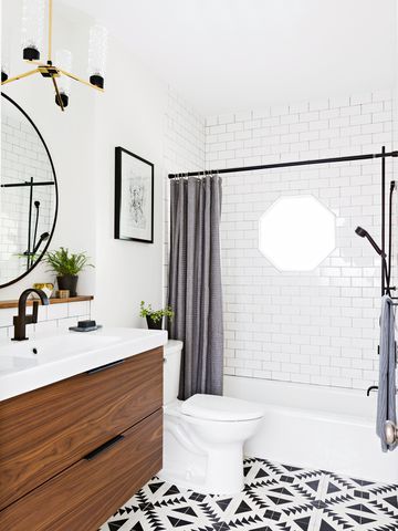 Compact Jersey City apartment bathroom with walnut vanity, subway tile tub surround and graphic floor